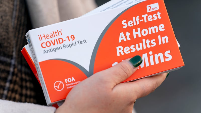 A woman holds two boxes of at-home Covid-19 test kits after waiting in a long line that snakes...