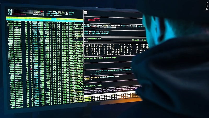 file photo of person wearing dark clothes in a dark room looking at computer code on a screen...